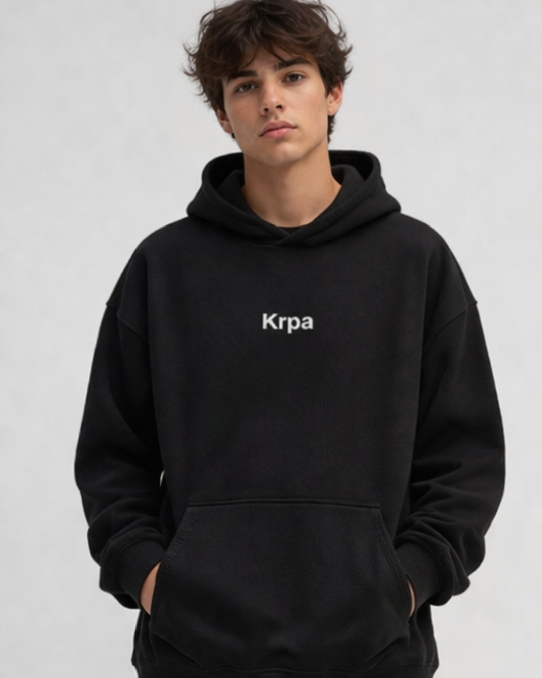 man wearing a black oversized hoodie with KRPA logo standing confidently on a plain background  