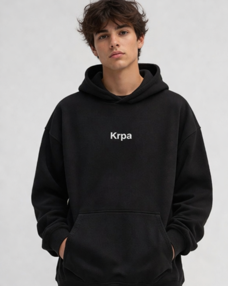 man wearing a black oversized hoodie with KRPA logo standing confidently on a plain background  