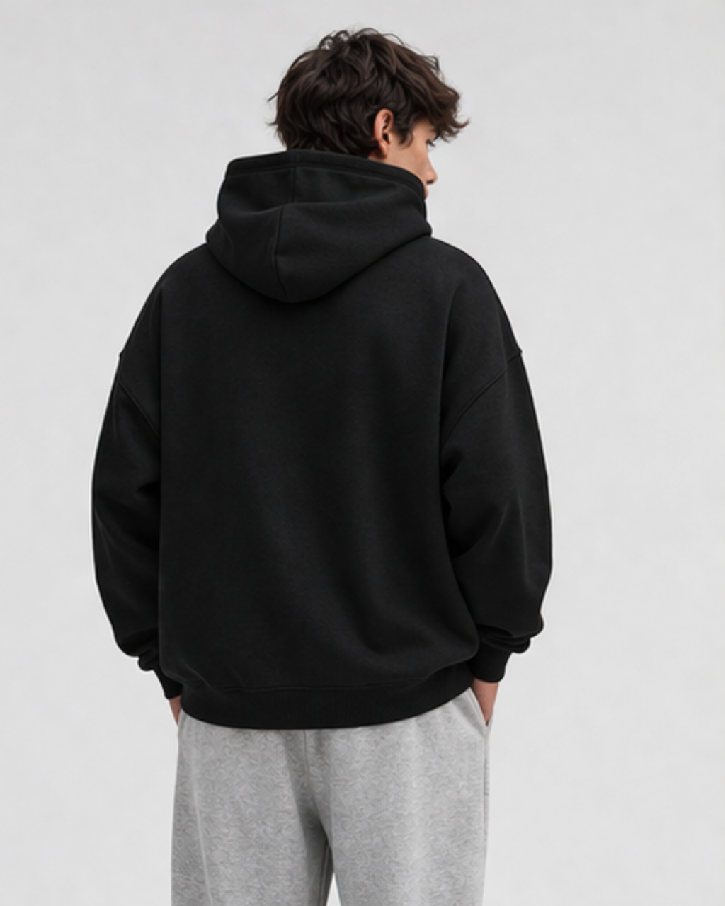Person wearing a black hoodie and gray pants on a white background