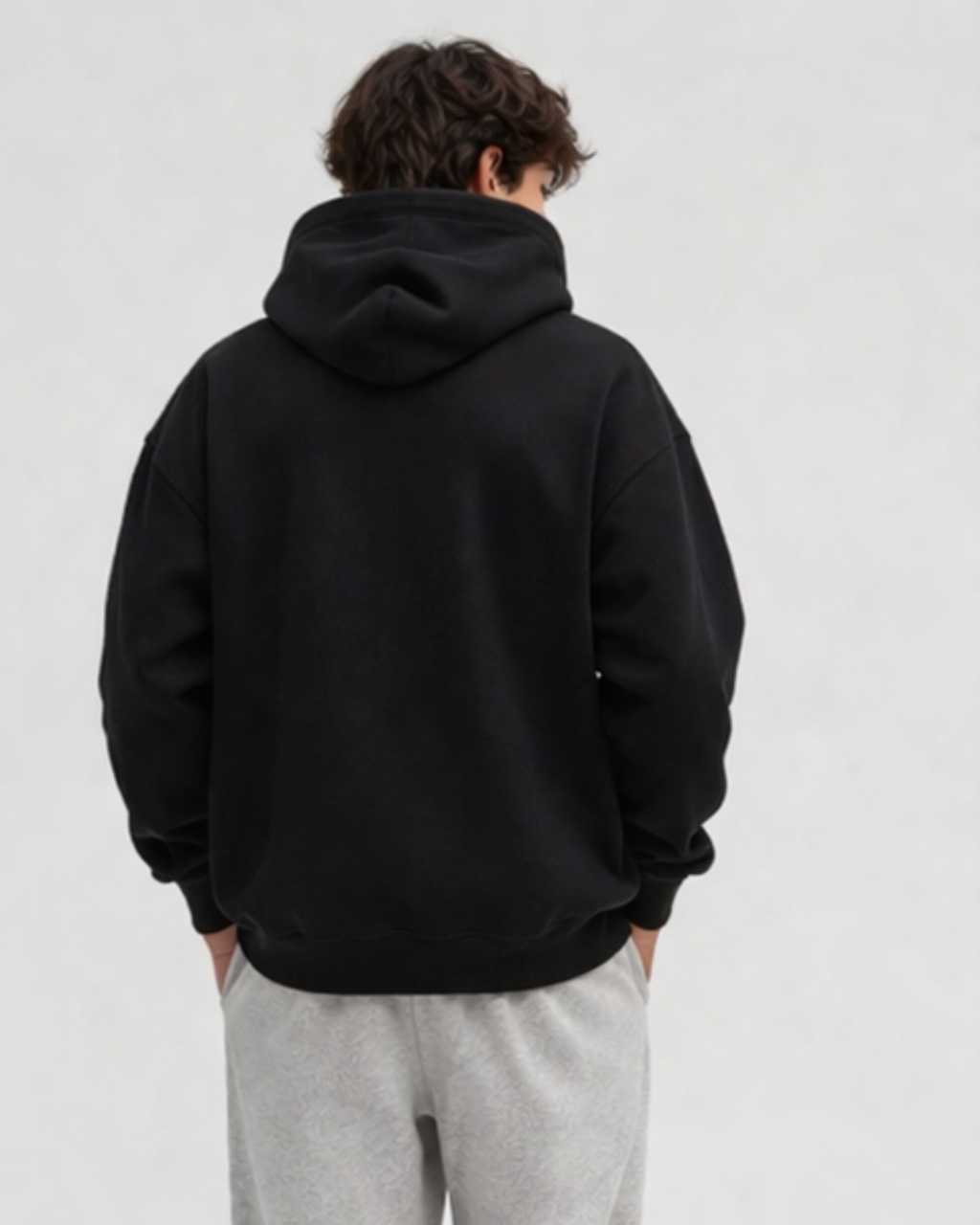 Person wearing a black hoodie and gray pants on a light gray background