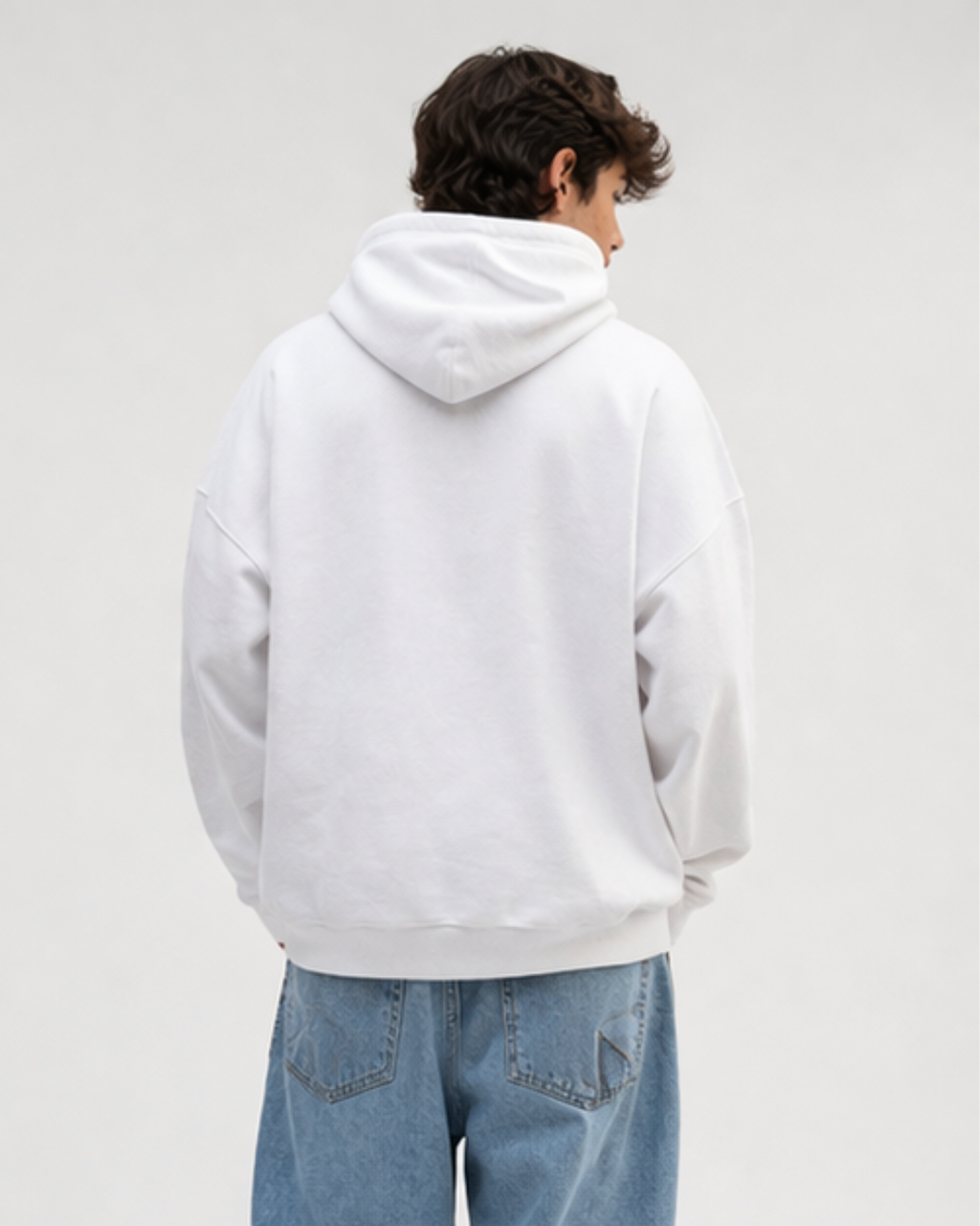 Person wearing a white hoodie and blue jeans on a plain background