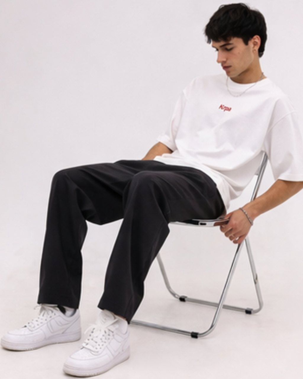Person sitting on a chair wearing a white t-shirt and black pants against a white background
