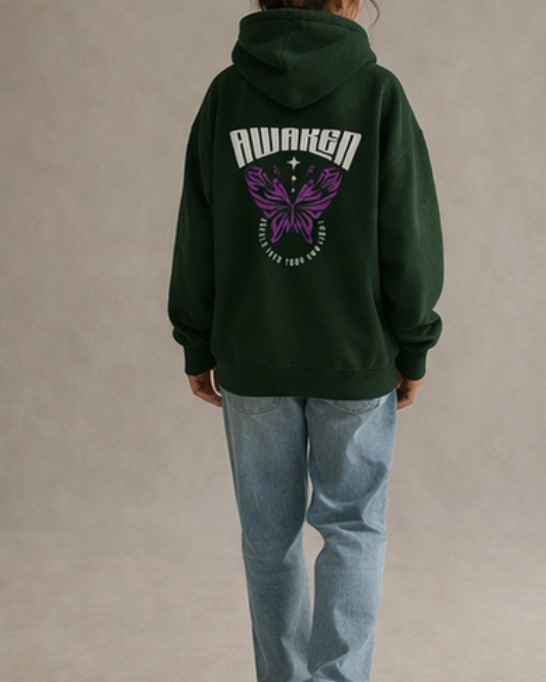 Person wearing a green hoodie with 'Awaken' and butterfly design on the back, standing against a beige background.