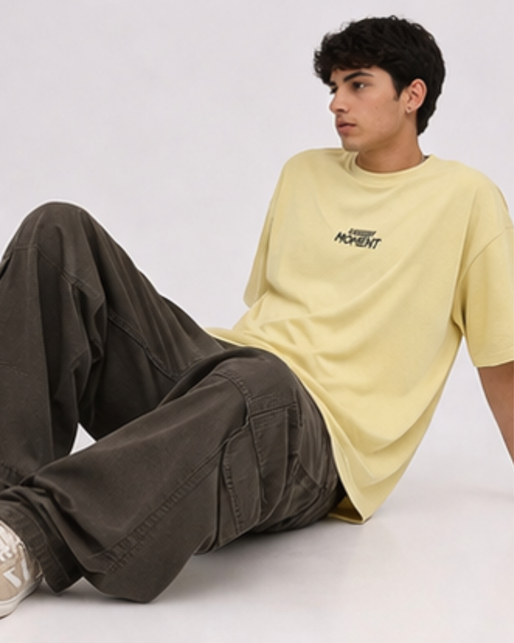 Person wearing a yellow t-shirt with text and dark pants sitting on a white floor.