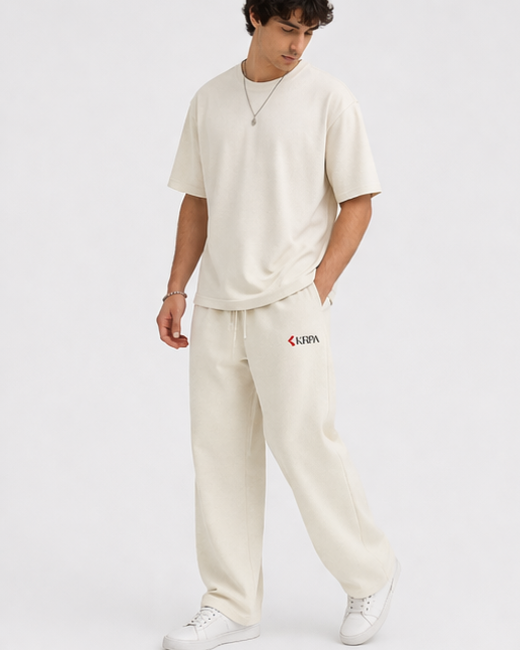 Person wearing off white outfit with KRPA logo on pants against a white background