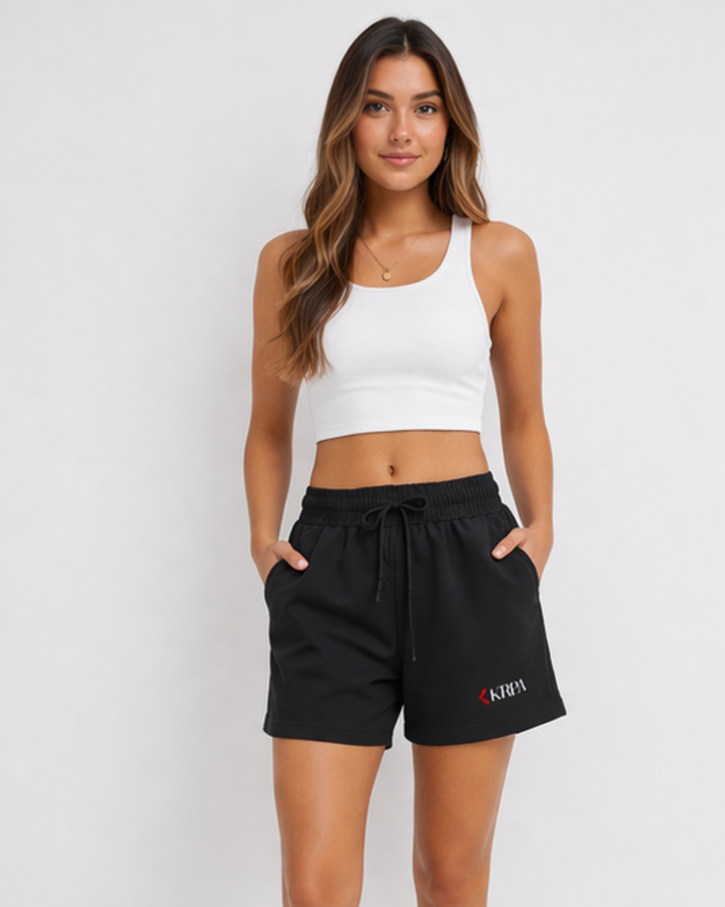 Woman wearing a white crop top and black shorts with KRPA logo on a plain background