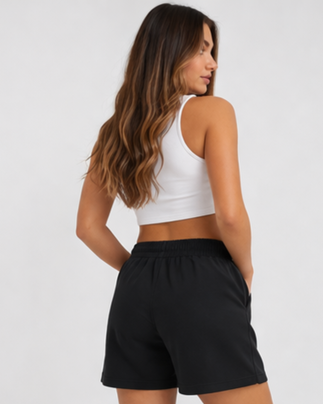 Woman wearing a white sports bra and black shorts on a plain background