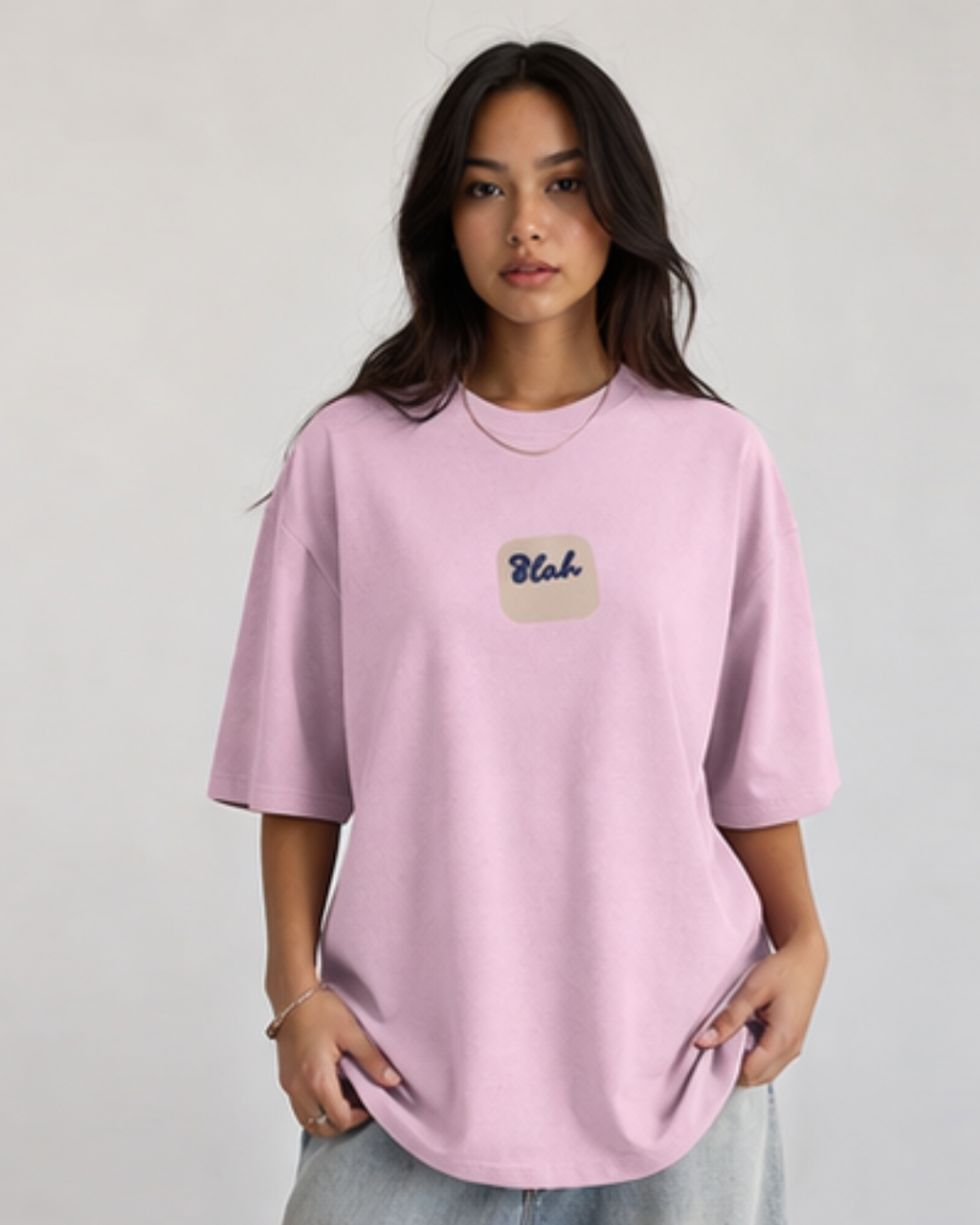 Woman wearing a light pink oversized t-shirt with 'Blah' written in the middle on a plain background