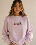 Person wearing a baby pink sweatshirt with 'Blessed' text on a plain background