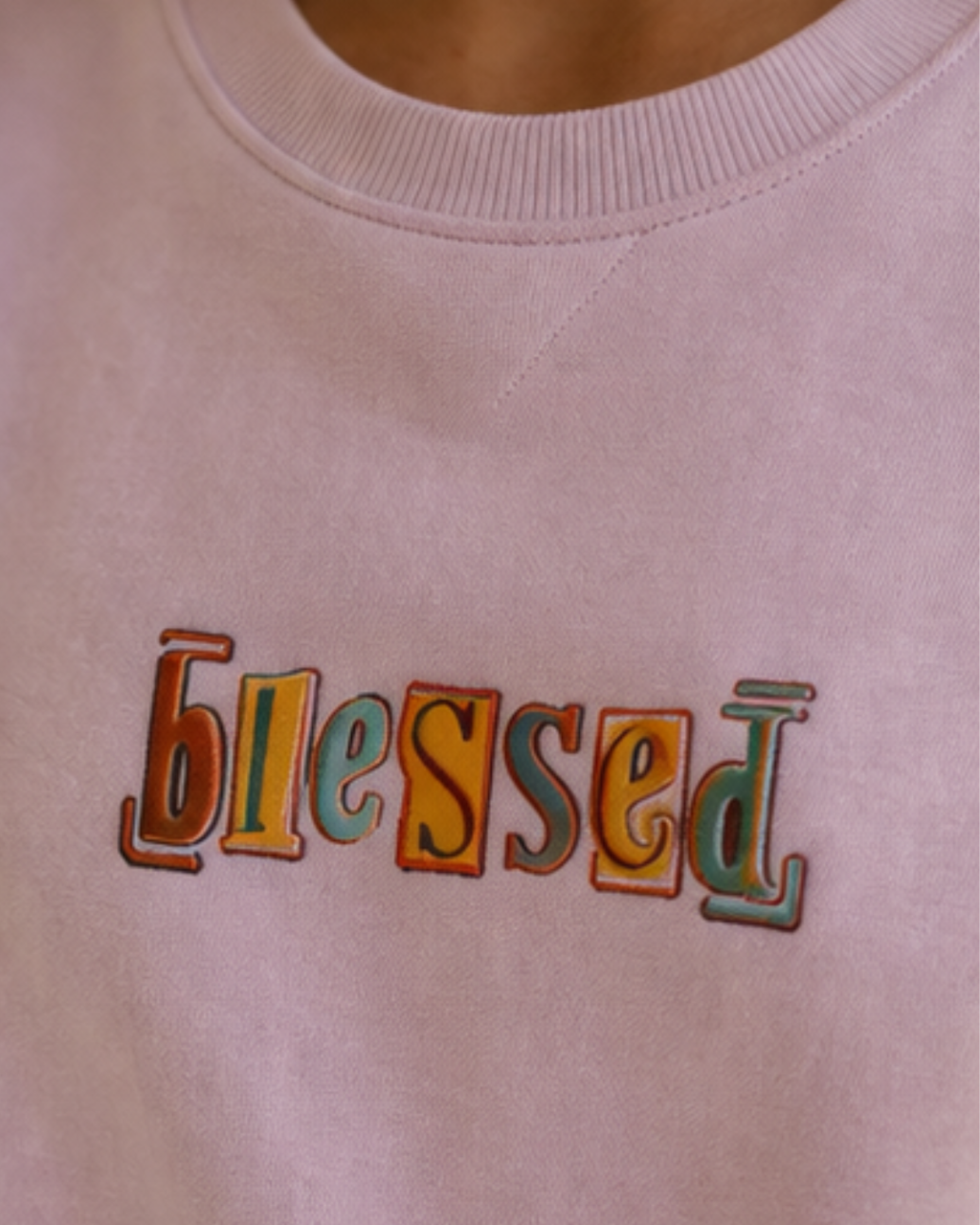 Light pink sweatshirt with 'blessed' in colorful letters on a plain background