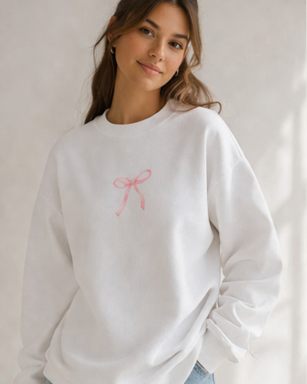 Woman wearing a white sweatshirt with a pink bow design on a plain background