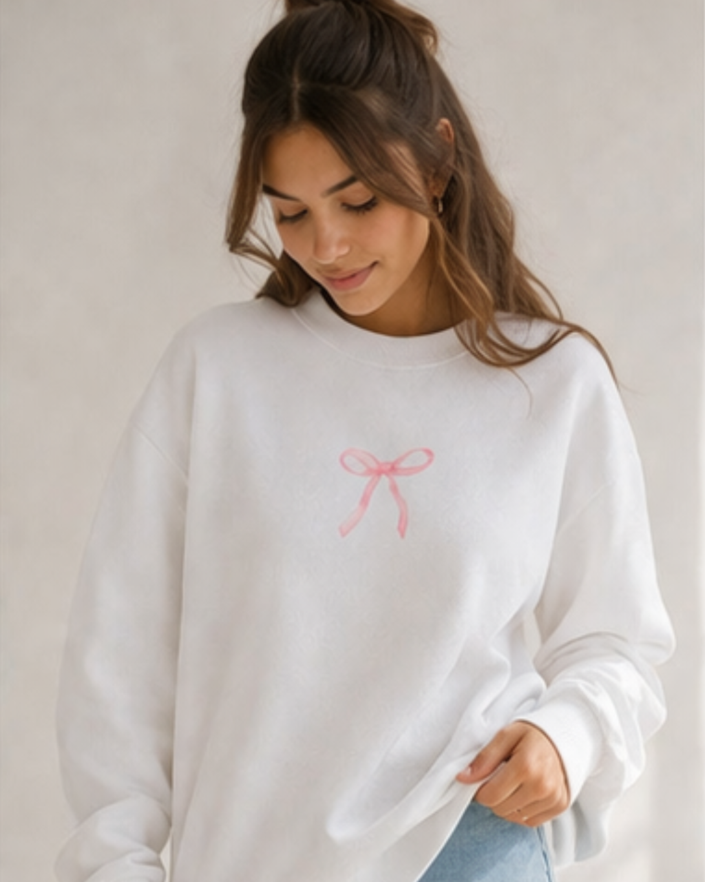 Woman wearing a white sweatshirt with a pink bow design on a plain background