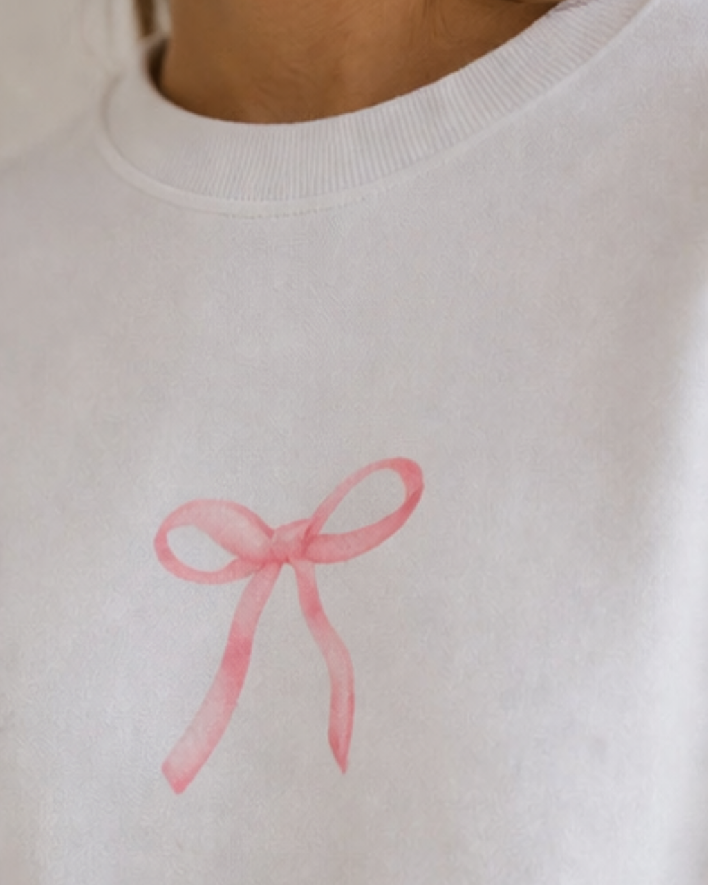 White sweatshirt with a pink bow design on a plain background