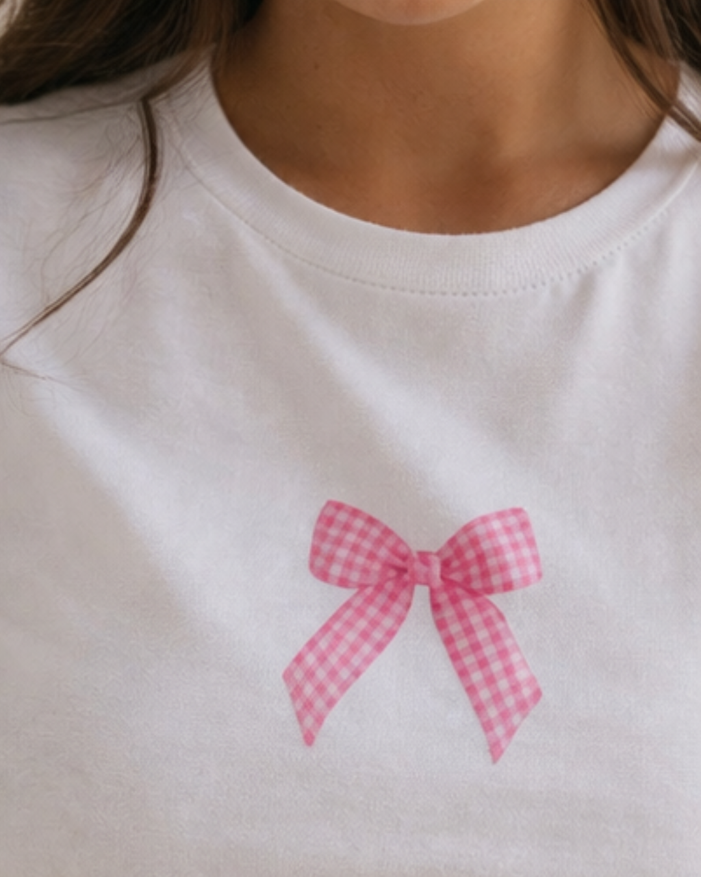 White shirt with a pink gingham bow design on a plain background