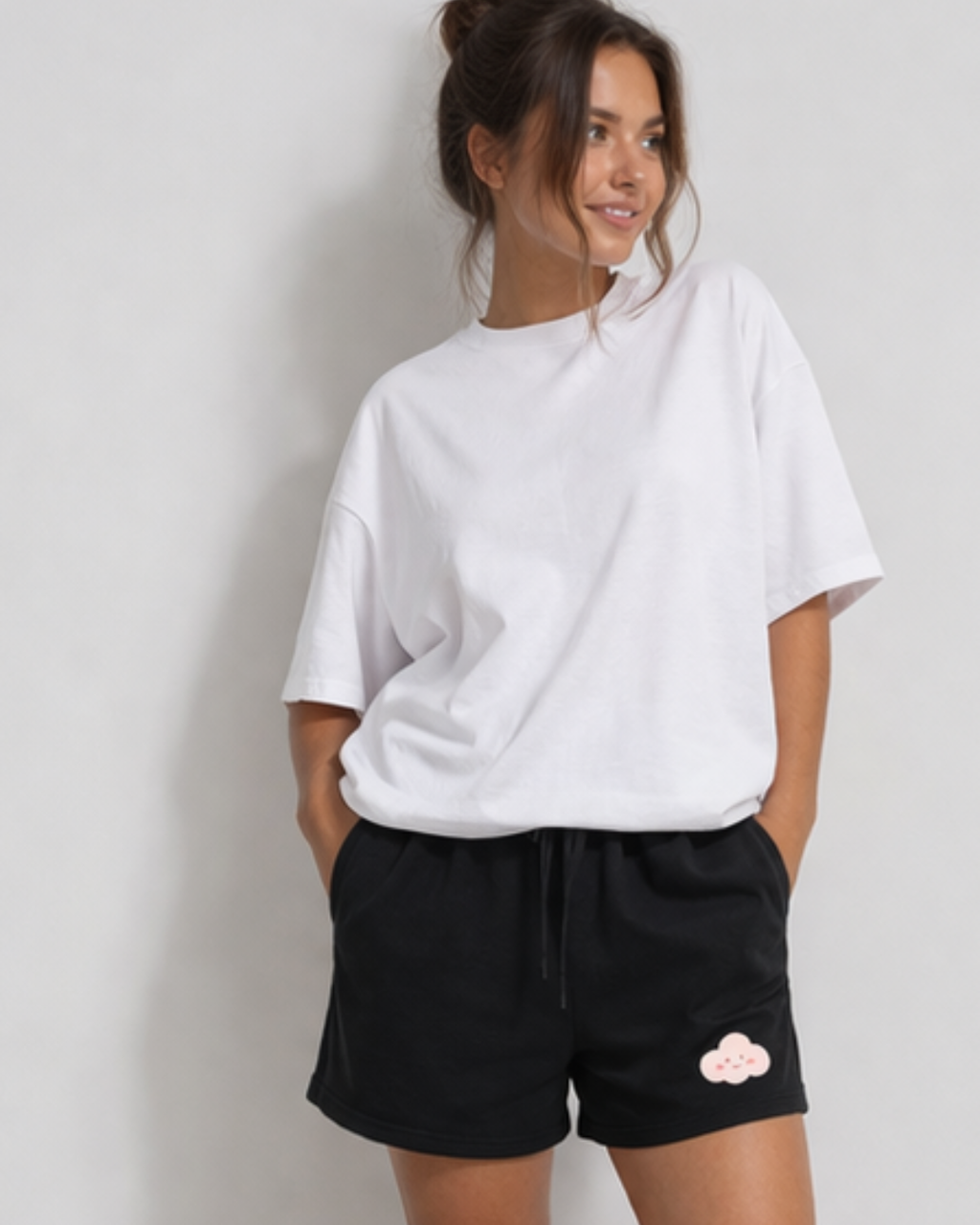 Woman wearing a white oversized t-shirt and black shorts with a cloud design on a plain background