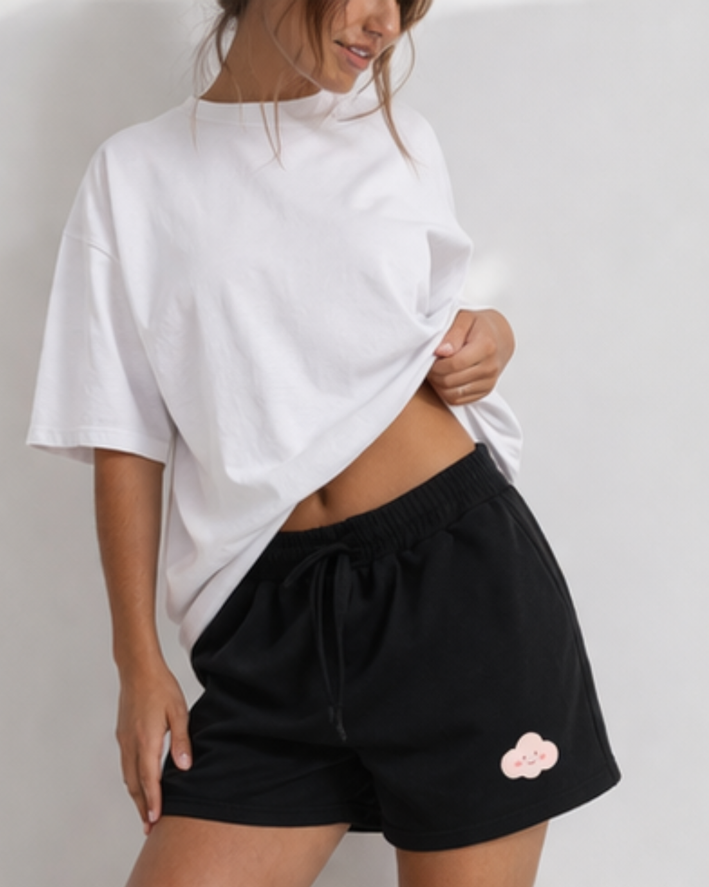 Person wearing a white oversized t-shirt and black shorts with a pink cloud design on a plain background