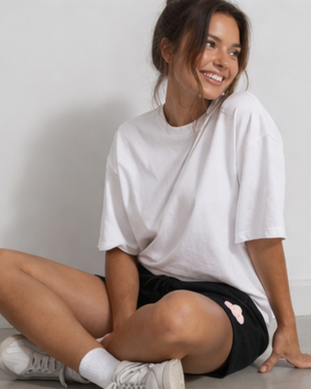 Woman wearing a white oversized t-shirt and black shorts sitting on the floor.