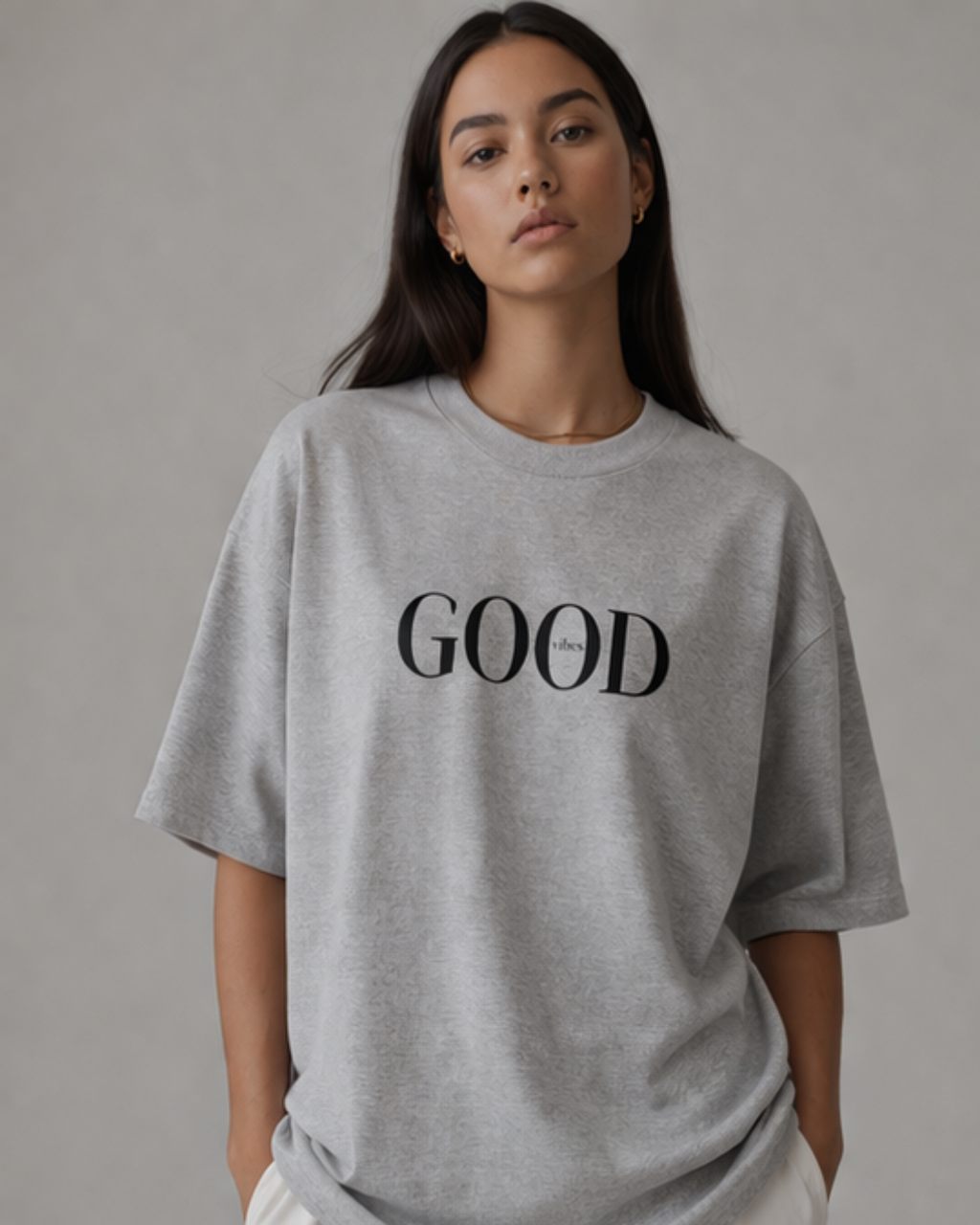 Person wearing a grey oversized t-shirt with 'GOOD' printed on it against a plain background