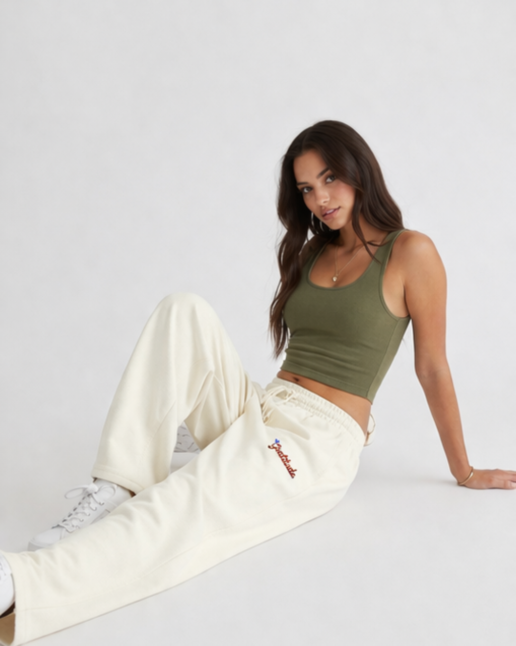 Woman wearing a green tank top and white pants sitting on a light gray background