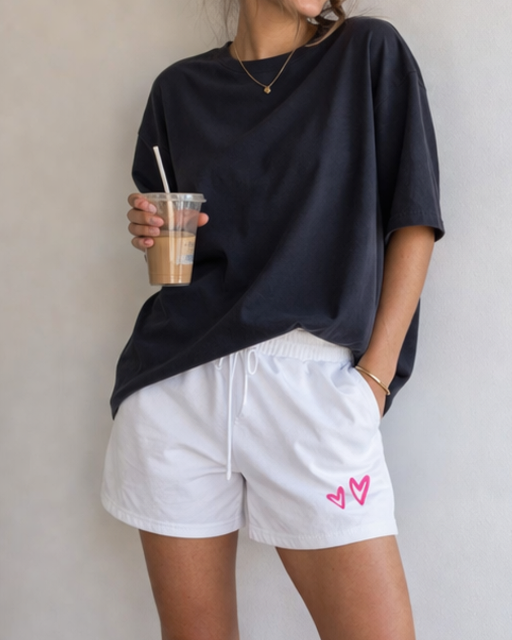 Person wearing a black oversized t-shirt and white shorts with pink hearts, holding a iced coffee.