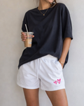 Person wearing a black oversized t-shirt and white shorts with pink hearts, holding a iced coffee.