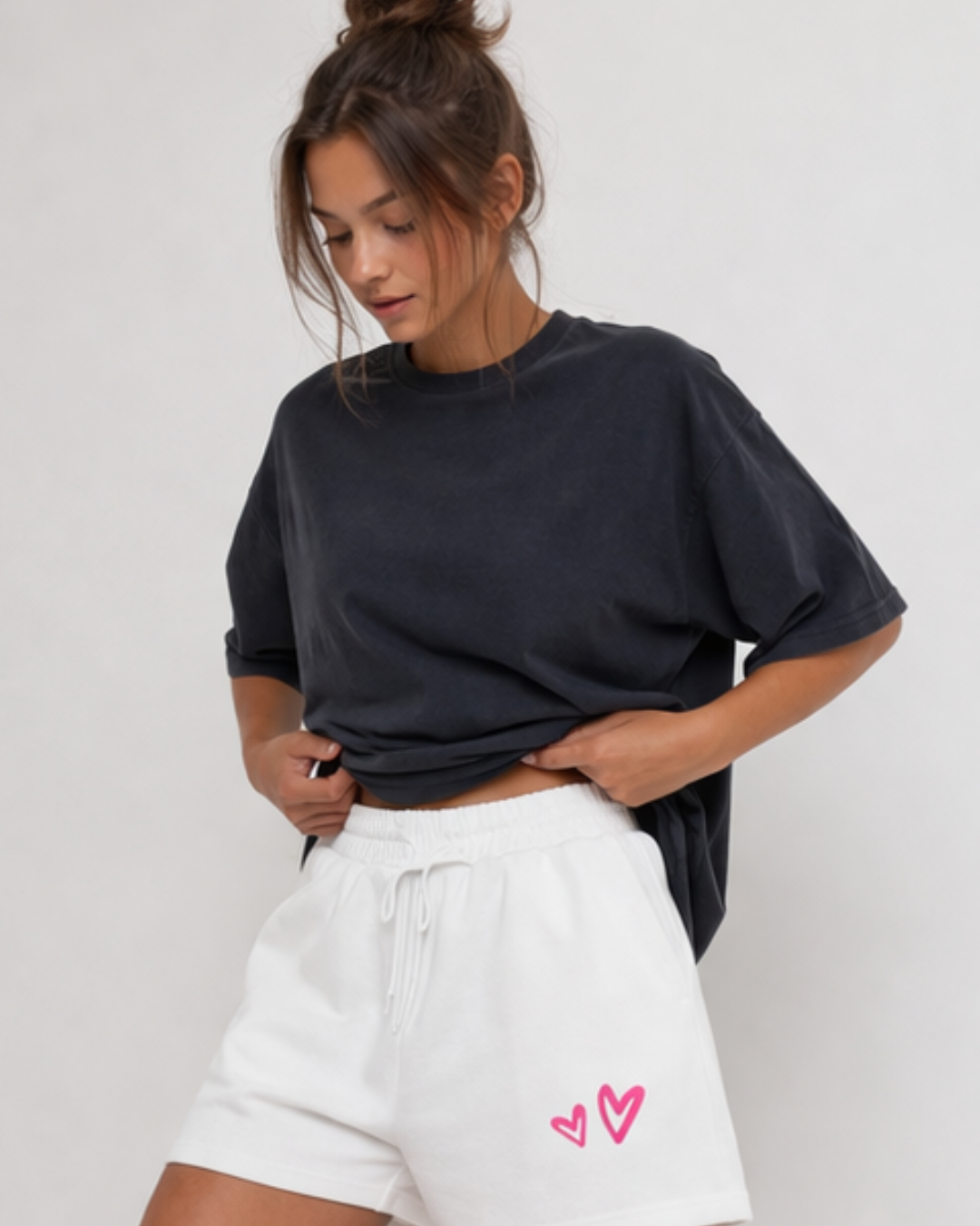 Woman wearing a black oversized t-shirt and white shorts with pink hearts on a plain background