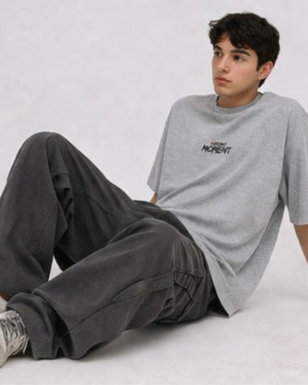 Person wearing a gray oversized t-shirt with text and dark pants on a light background