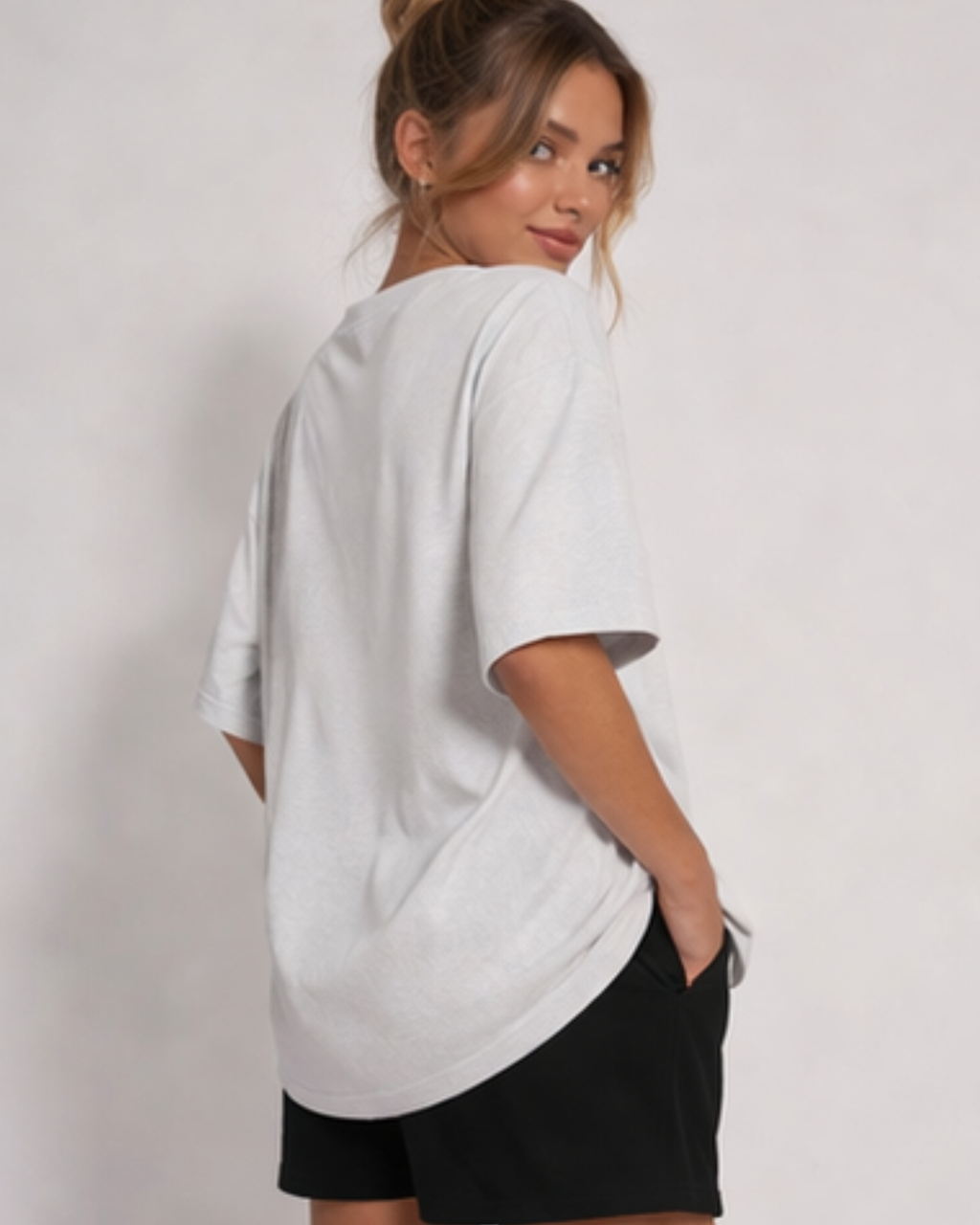 Woman wearing an oversized light gray t-shirt and black shorts on a plain background