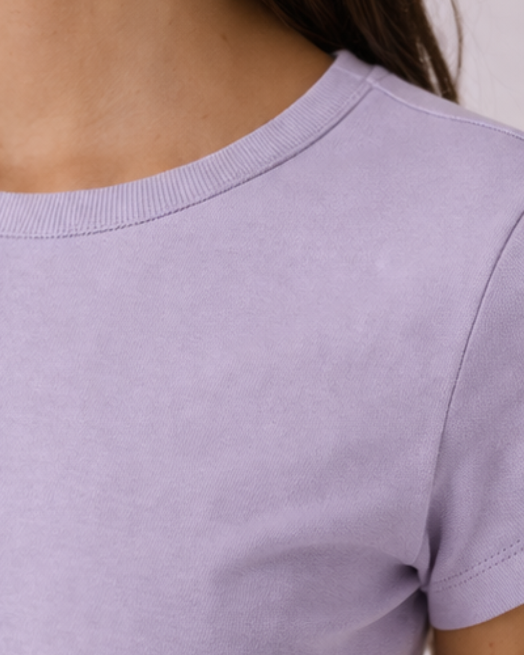 Close-up of a person wearing a light purple t-shirt with a neutral background