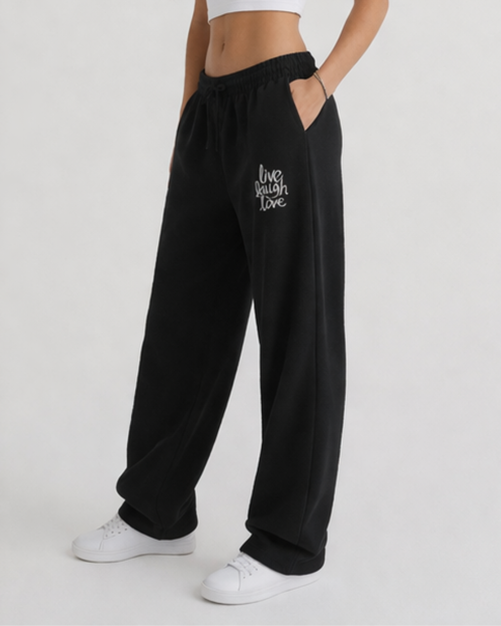 Black sweatpants with 'live laugh love' text worn by a person on a white background