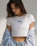 Woman wearing a white crop top with 'loved' text, holding a light blue denim jacket.