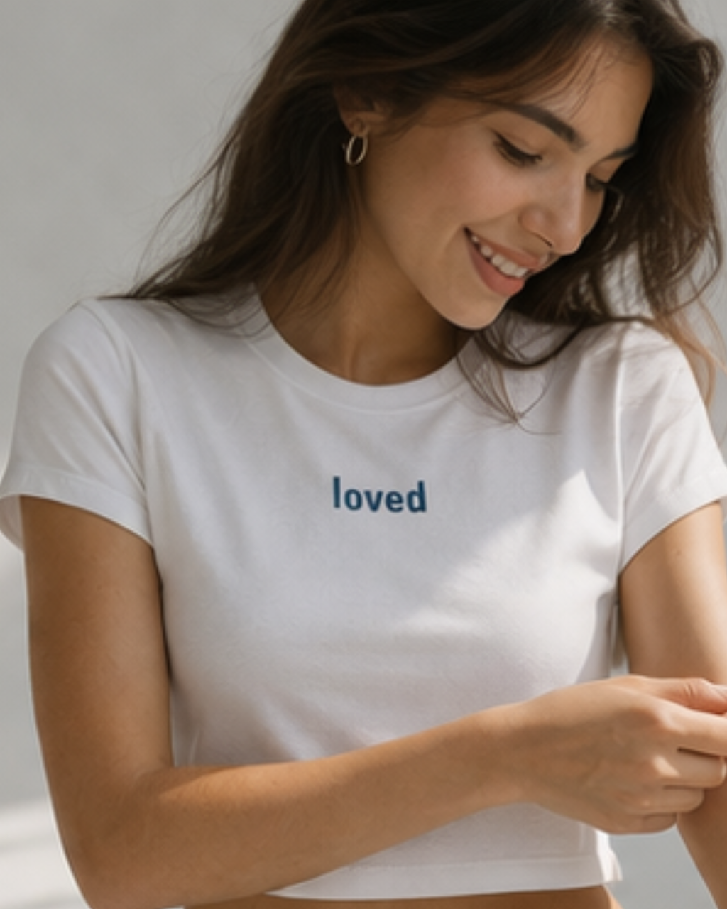 Woman wearing a white cropped t-shirt with 'loved' text on a plain background.