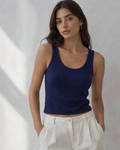Woman wearing a navy tank top and white pants against a neutral background