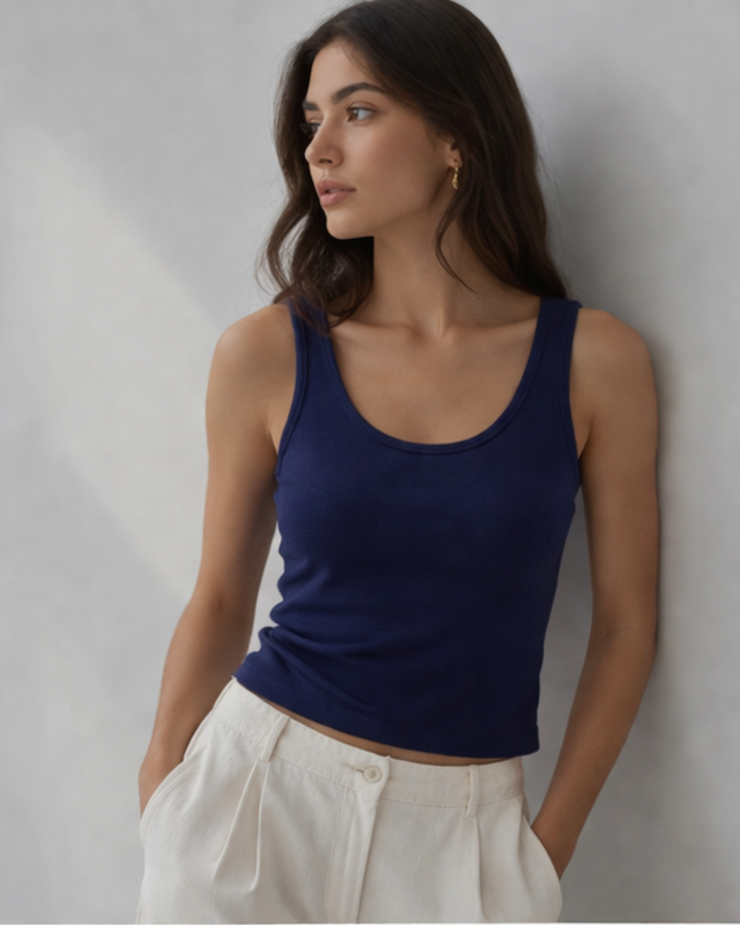 Woman wearing a blue tank top and white pants against a plain background