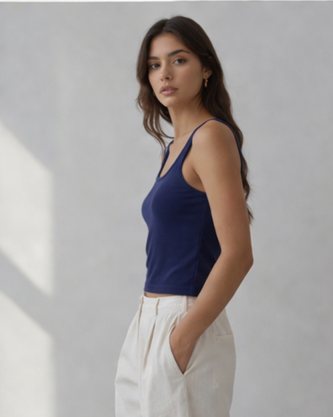 woman wearing blue tank top styled with white pant standing on a light background 