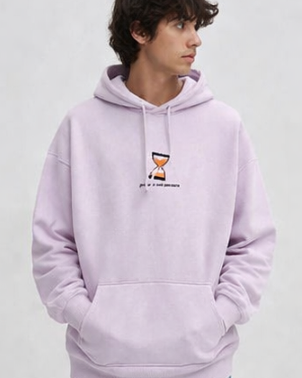 Person wearing a baby pink hoodie with a small graphic and text on a plain background