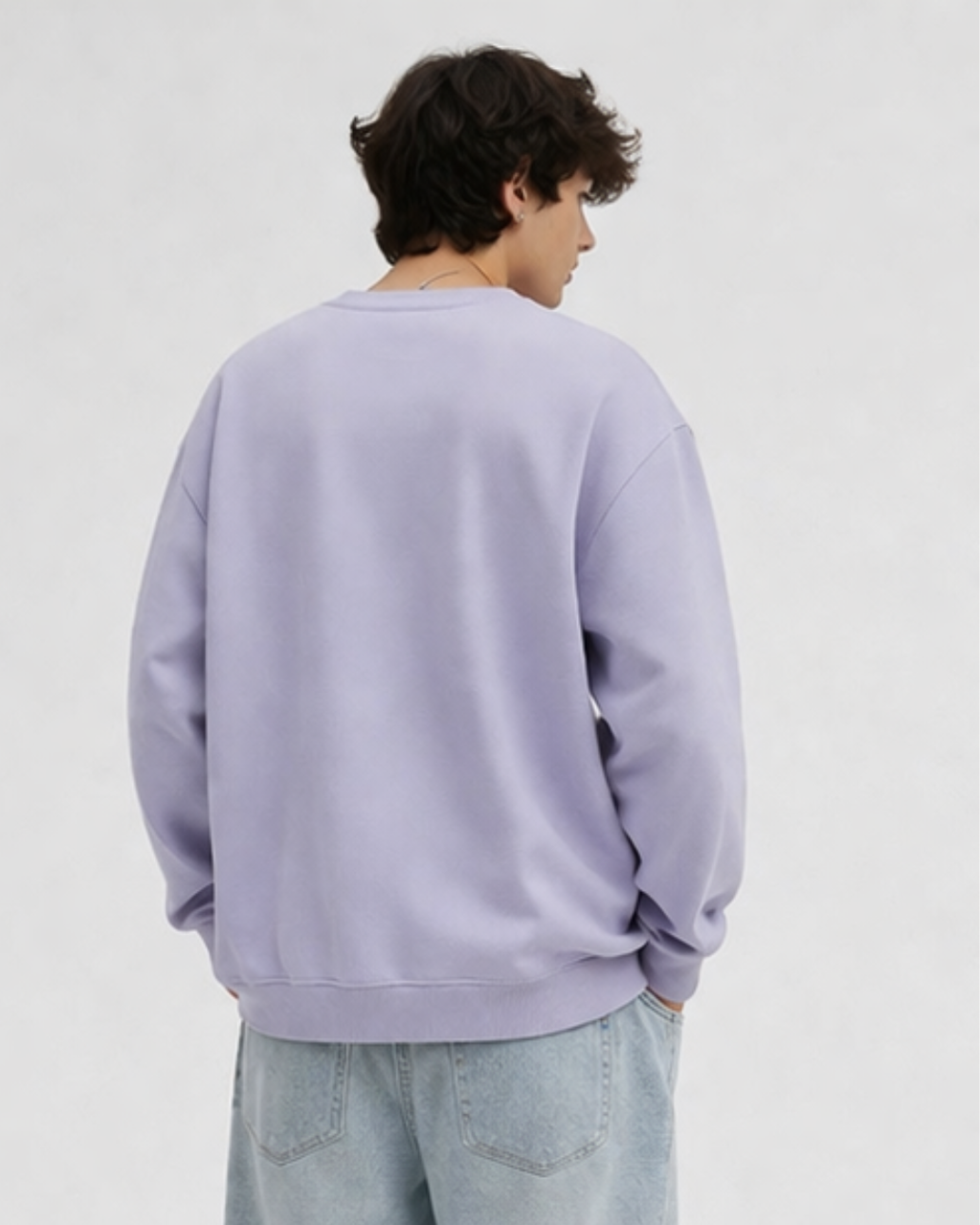 Person wearing a light purple sweatshirt and light blue jeans on a plain background