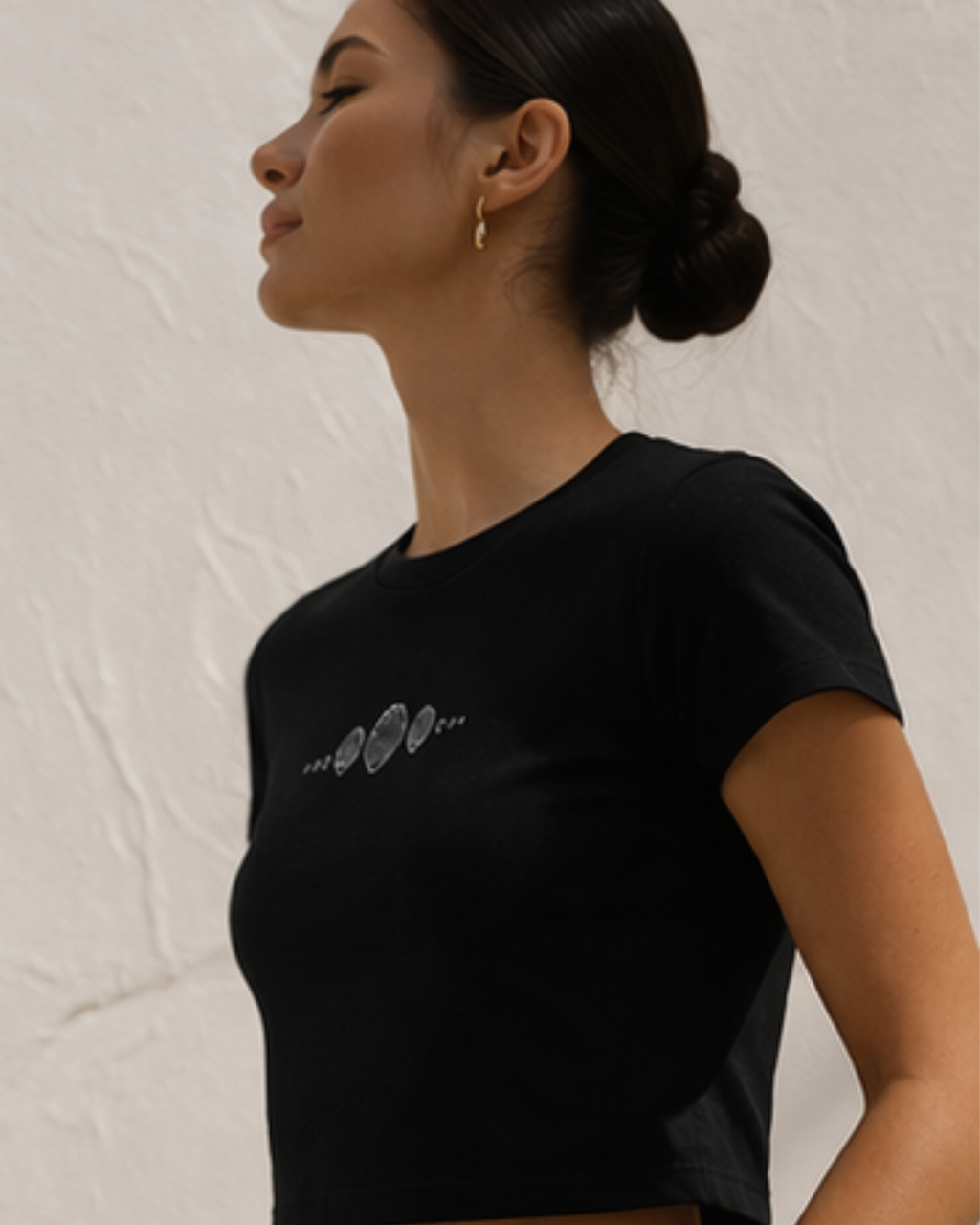 Woman wearing a black baby t-shirt with a logo on a light background