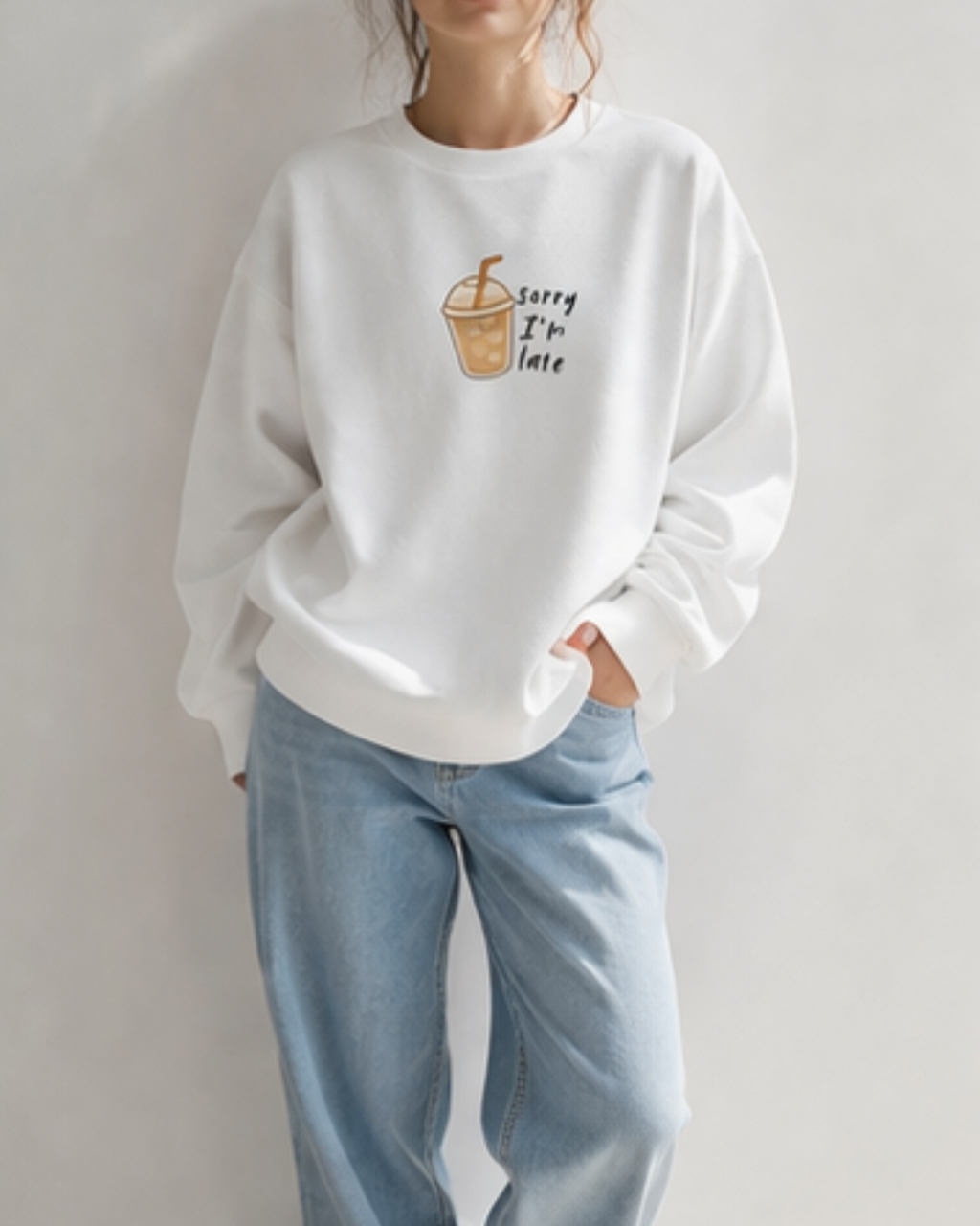 Person wearing a white sweatshirt with a coffee cup graphic and text, standing against a plain background.