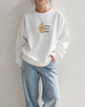 Person wearing a white sweatshirt with a coffee cup graphic and text, standing against a plain background.