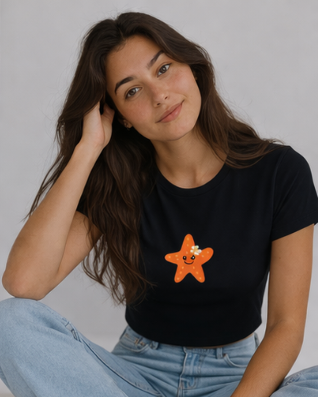 Woman wearing a black t-shirt with an orange starfish design on a plain background