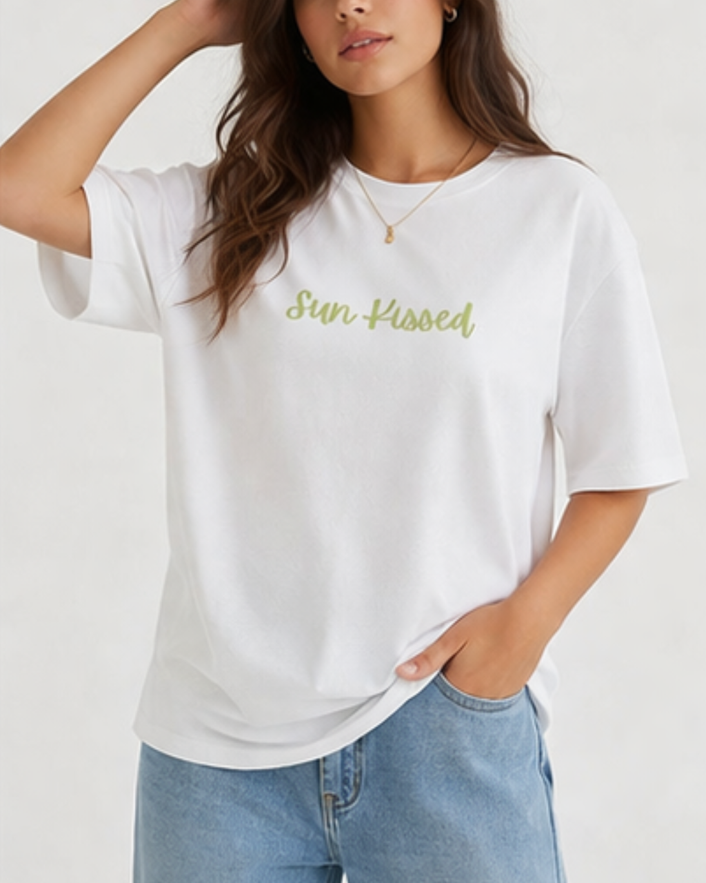 Woman wearing a white t-shirt with 'Sun Kissed' text and blue jeans on a plain background