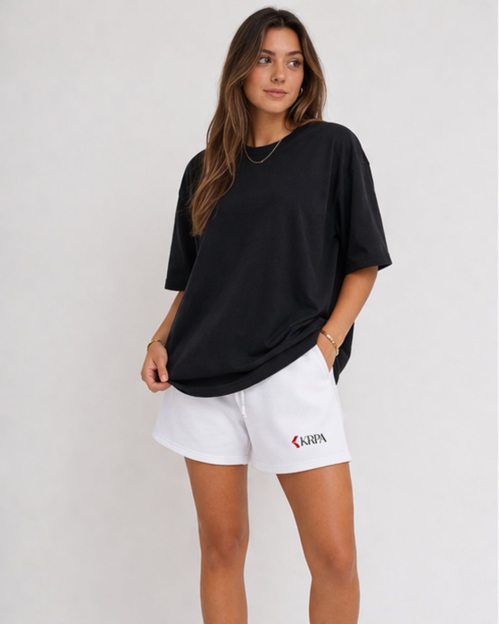 Woman wearing a black oversized t-shirt and white shorts with KRPA logo on a plain background