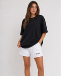 Woman wearing a black oversized t-shirt and white shorts with KRPA logo on a plain background