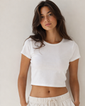 Woman wearing a white crop top and white pants against a plain background