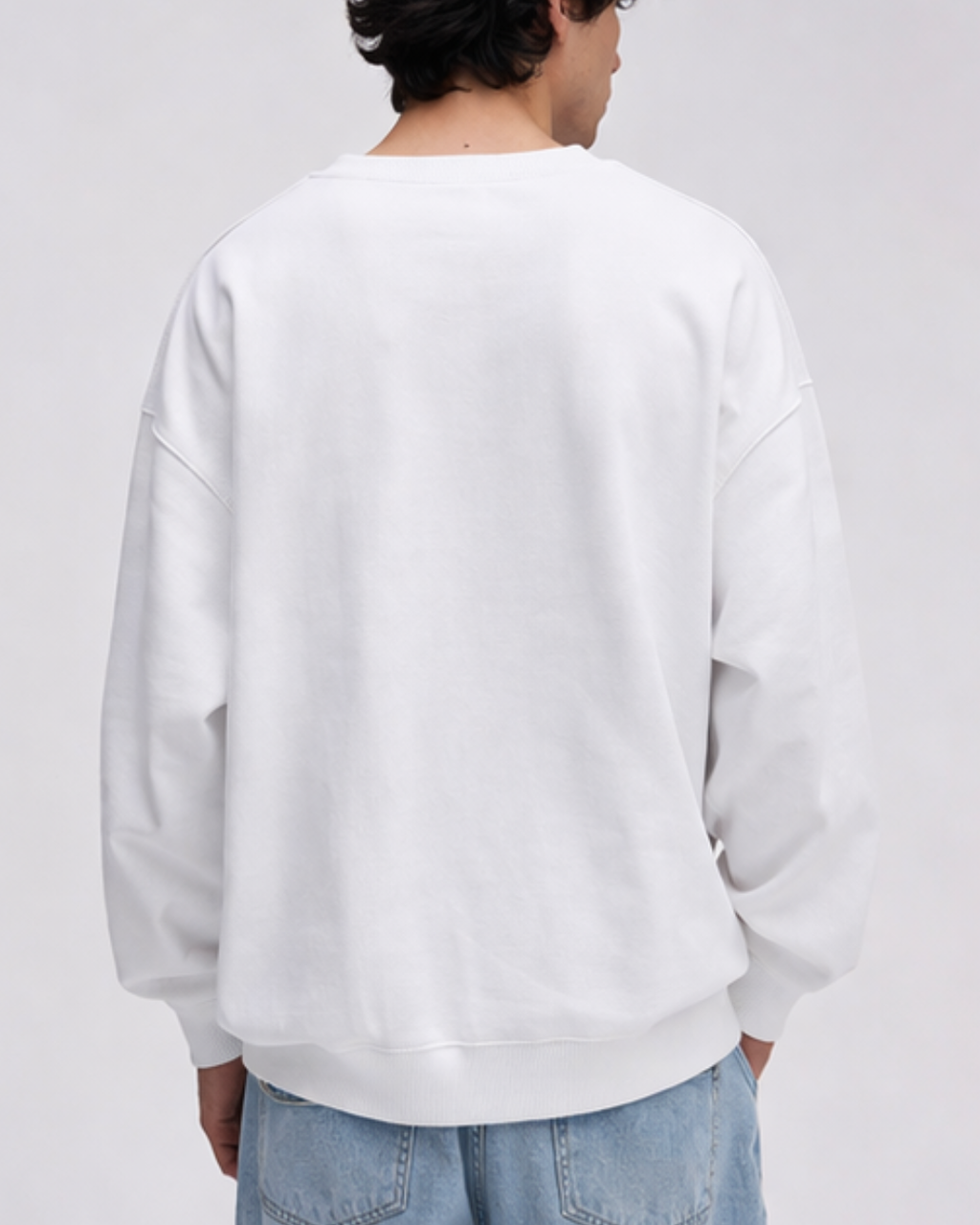 Person wearing a plain white sweatshirt and light blue jeans on a gray background