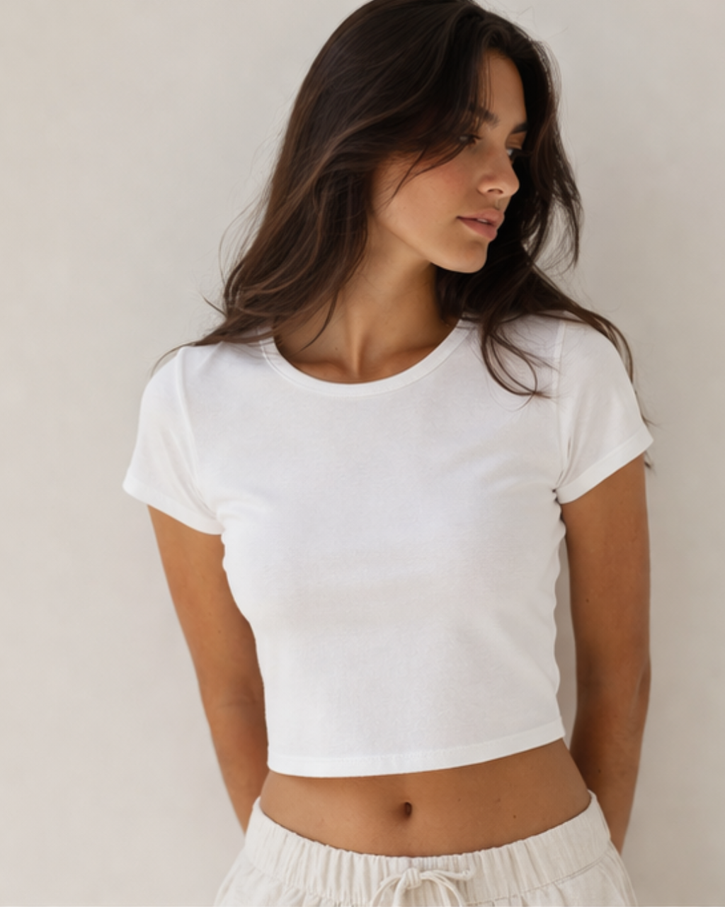 Woman wearing a white crop top against a plain background