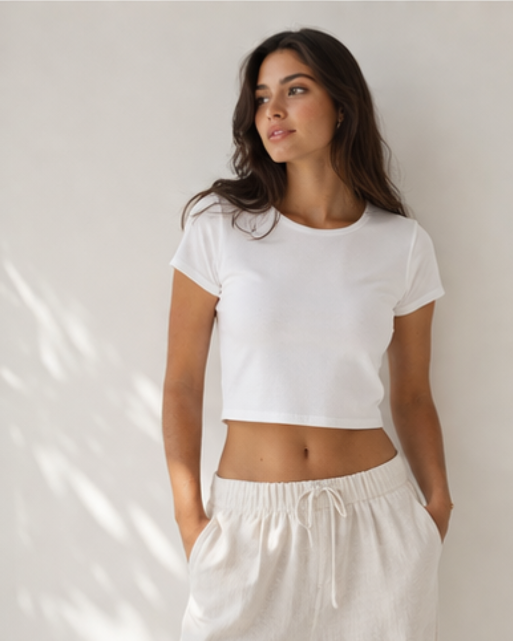 Woman wearing a white crop top and white pants against a neutral background