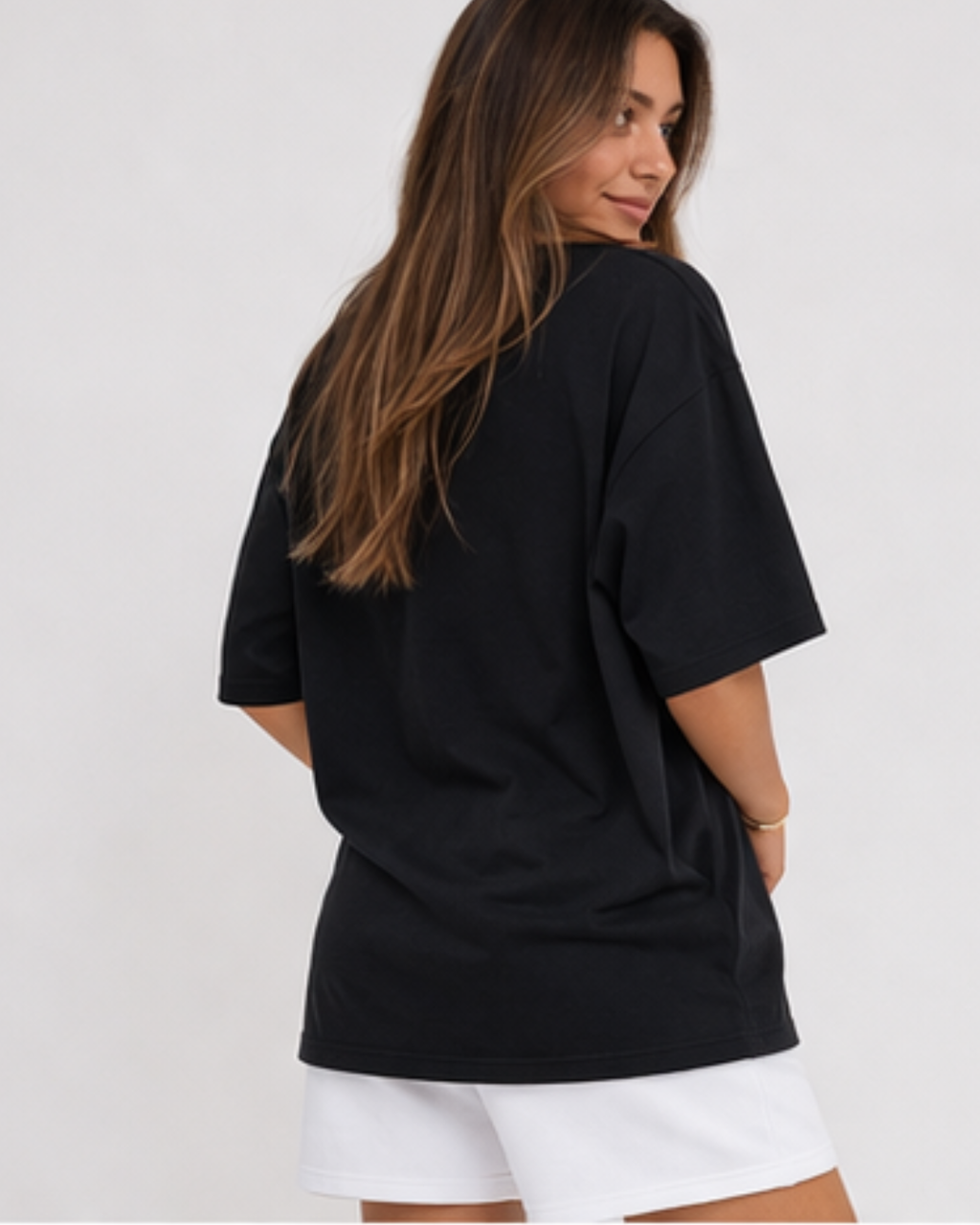 Woman wearing a black oversized t-shirt and white shorts on a plain background