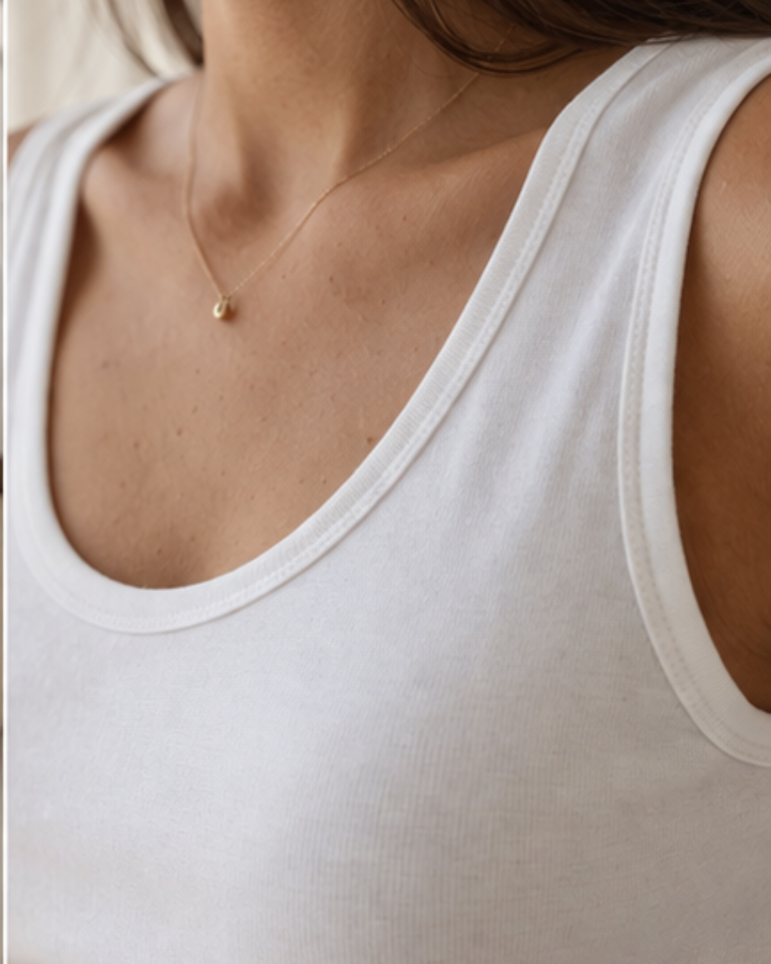 Close-up of a person wearing a white tank top and a delicate necklace with a small pendant.